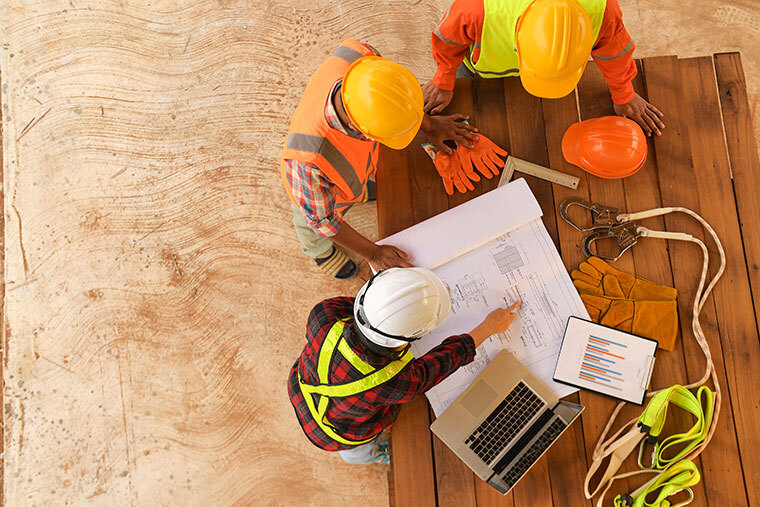 3 men in hardhats at table looking at construction plans