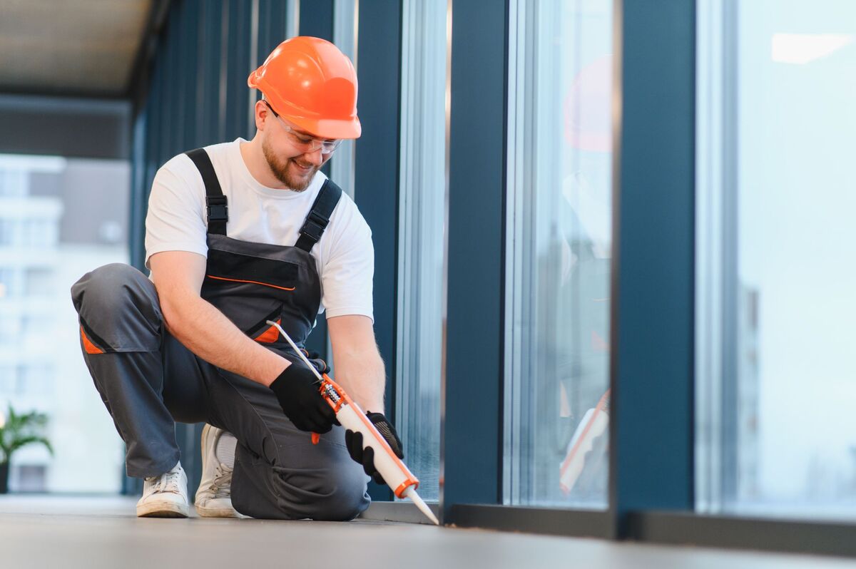 Man applying sealant around window at floor