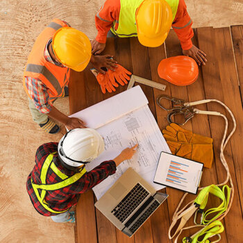3 men in hardhats looking at plans on construction site